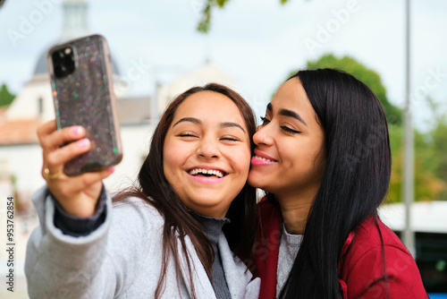 Happy Latin lesbian couple hugging, laughing and taking a selfie at street. LGBT couple.