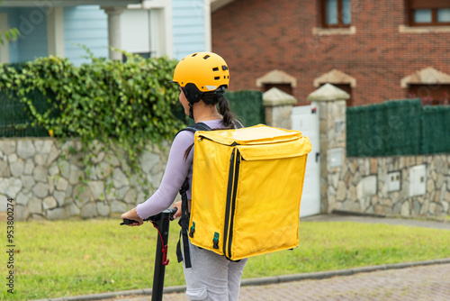 Latin food delivery girl with yellow backpack and helmet riding an electric scooter, rear view photo