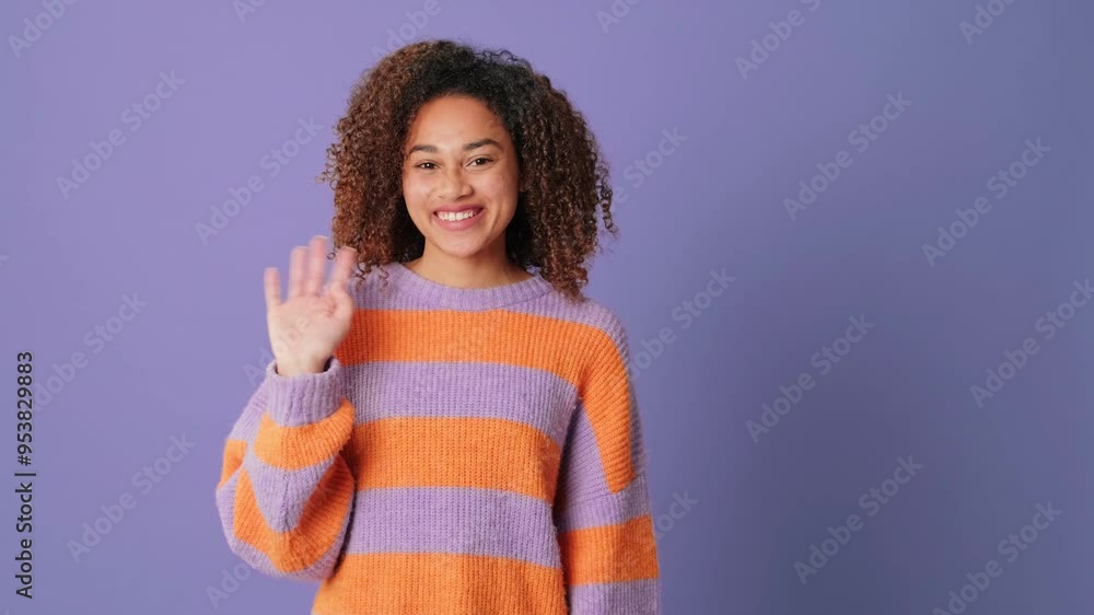 Happy young woman waving palm, greeting gesture looking at camera on lilac background in studio Happy young woman waving palm, greeting gesture looking at camera on lilac background in studio
