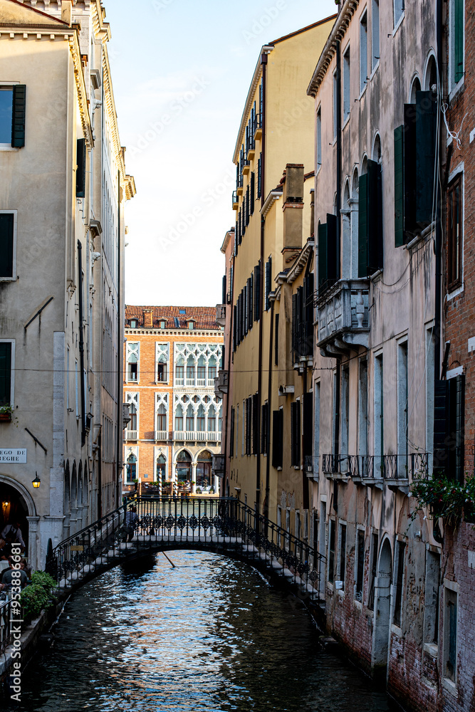 Naklejka premium Charming narrow canal in Venice with picturesque buildings and a classic bridge on a sunny afternoon