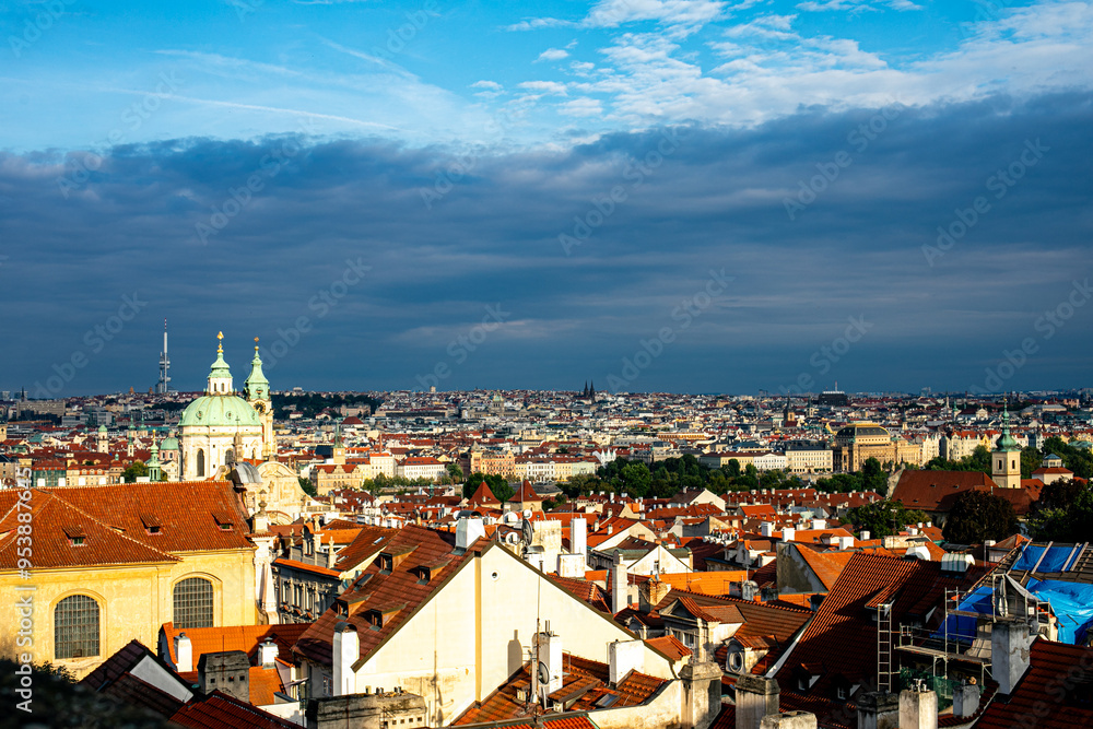 Fototapeta premium Panoramic view of rooftops and historical architecture in Prague under a vibrant sky at sunset
