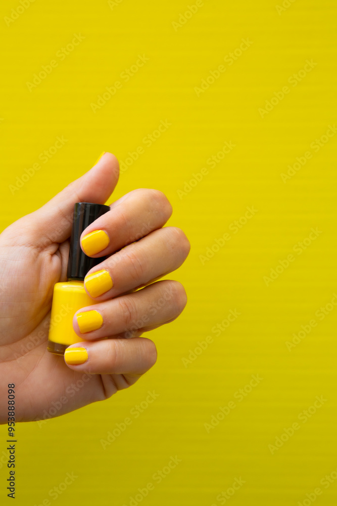 Woman's hand with yellow nails holding a bottle of nail polish. Woman's hand with yellow nails holding a bottle of nail polish.