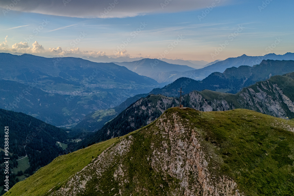 Naklejka premium Aerial view of a mountain ridge at sunset with lush green slopes and distant peaks in the distance