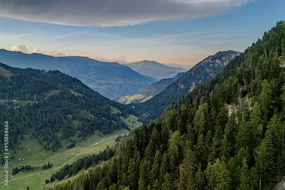 Fototapeta premium Wide view of lush green mountains under a colorful sky during sunset in the Alps