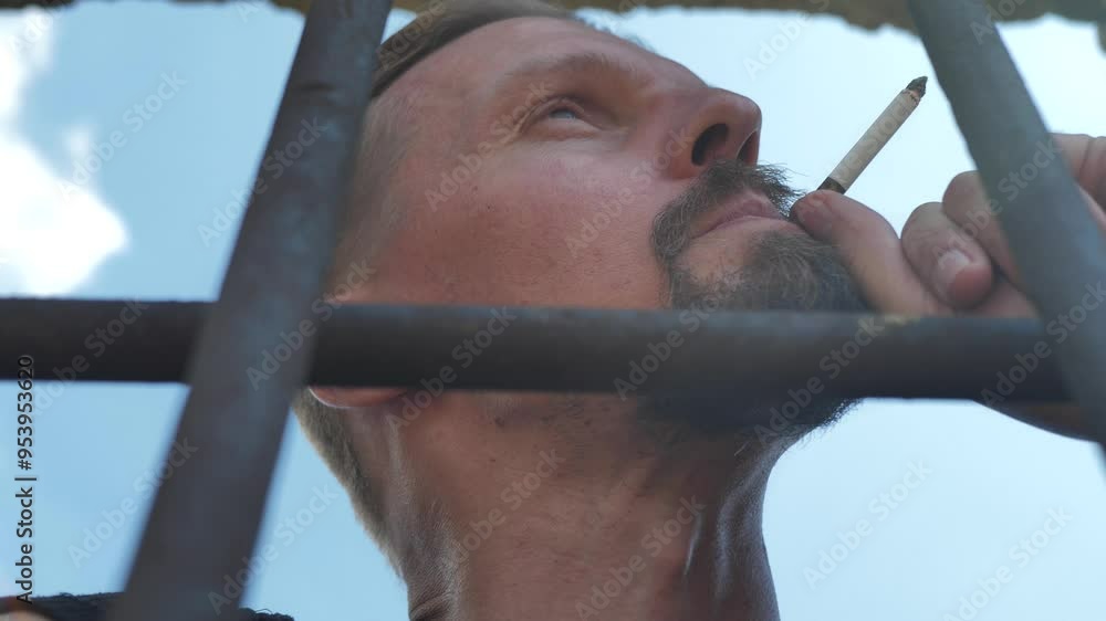 Looking up: A young inmate with a beard takes a drag on a cigarette ...