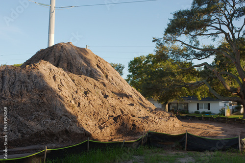 Wide view near sunset large dirt pile on the right of Electric Substation with High Power Lines in St. Petersburg, Florida. Temporary Silt Fencing, green grass, blue sky and white clouds , with large 
