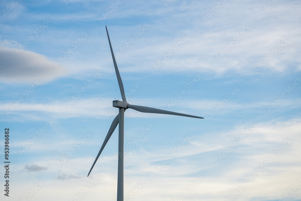 A wind turbine is standing tall in the sky, with a blue sky behind it
