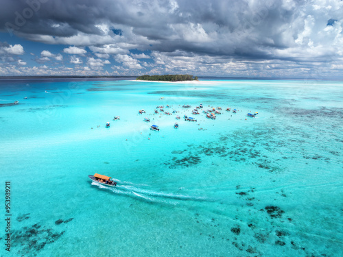 Aerial view of colorful boats in clear azure water in summer. Mnemba island, Zanzibar. Top view of sandbank in low tide, blue sea, white sand, swimming people, yachts, dramatic sky with clouds. Ocean photo