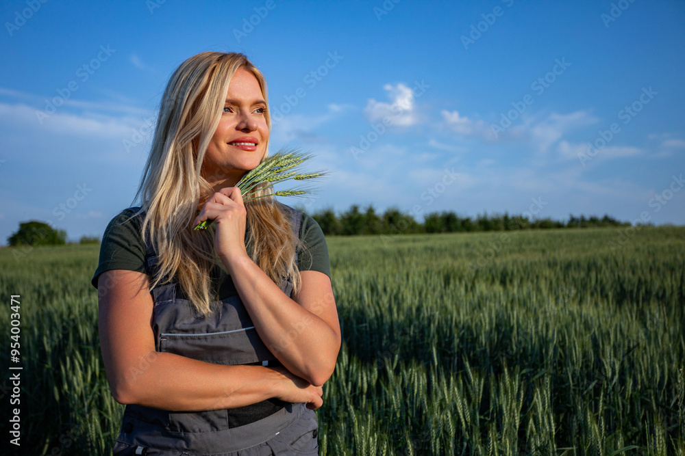 Satisfied and smiling female farmer standing in a grain field, holding wheat stalks near her face Satisfied and smiling female farmer standing in a grain field, holding wheat stalks near her face