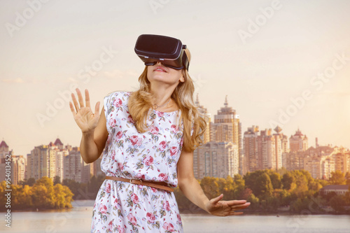 Portrait of amazed blonde mature woman in vr headset outdoors. City river in the background. photo