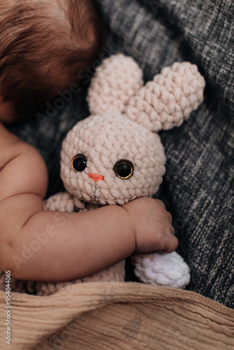 Sweet tiny newborn baby's hand hugging stuffed beige rabbit toy photo