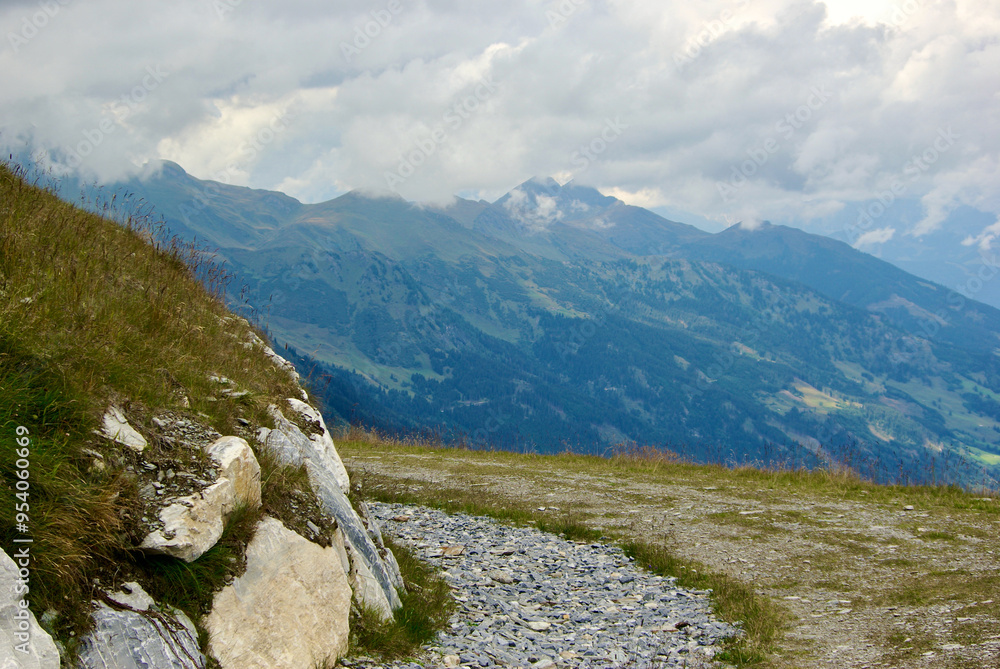 Obraz premium View of an amazing mountain landscape with a stony path on a hazy day with gray clouds and fog over the peaks in autumn in Austria.