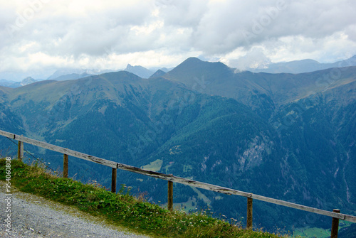 View of a mountain landscape with a village in the valley below a wooden fence on a hazy day with gray clouds and fog over the peaks in autumn in Austria.