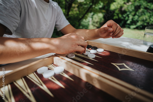 Konstfotografi Hands move pieces across a wooden backgammon board during a relaxing game outside on a sunny day
