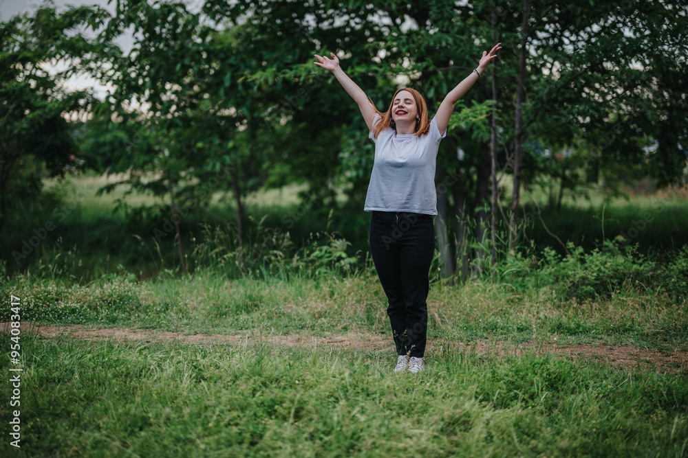 A happy woman stands with arms raised, enjoying the fresh air in a vibrant green park setting. A happy woman stands with arms raised, enjoying the fresh air in a vibrant green park setting.