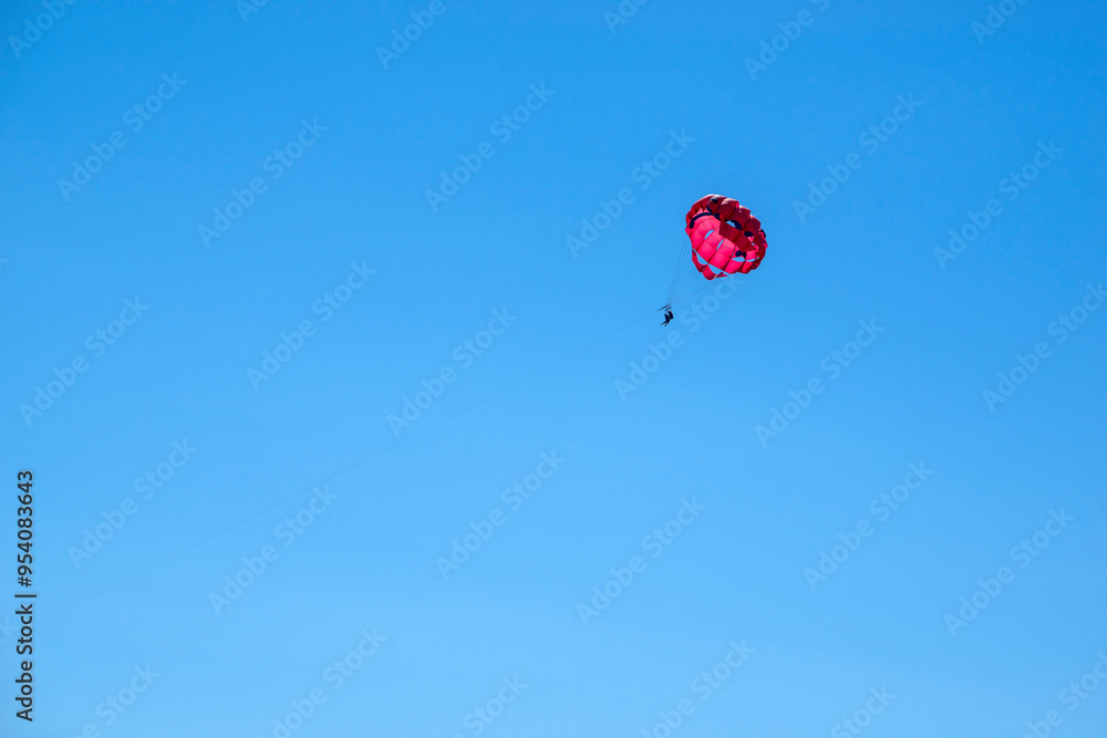 Two persons silhouettes doing parasailing on a blue sky Two persons silhouettes doing parasailing on a blue sky