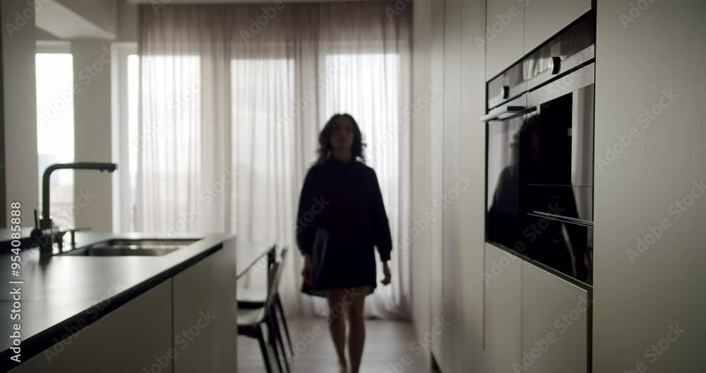 A dimly lit image capturing the silhouette of a young woman walking in a stylish, modern kitchen with contemporary appliances. Silhouette of a Young Woman Walking Through a Modern Kitchen A dimly lit image capturing the silhouette of a young woman walking in a stylish, modern kitchen with contemporary appliances. Silhouette of a Young Woman Walking Through a Modern Kitchen