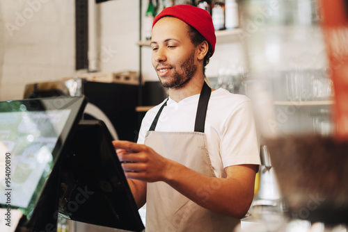 Smiling barista, Latin man in red hat taking order on digital pos system photo