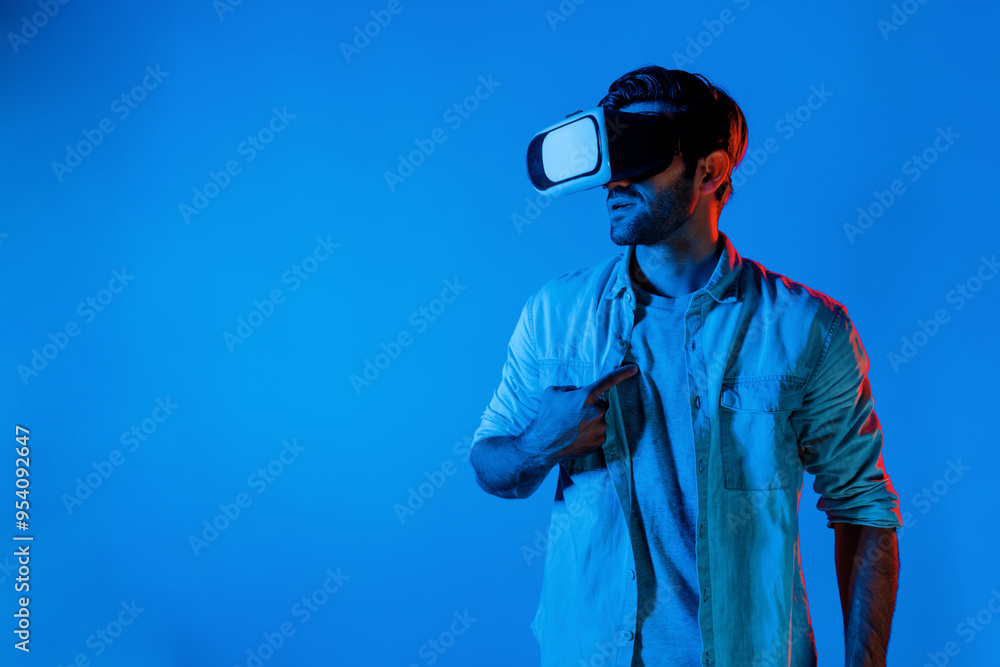 Caucasian man with casual cloths wearing VR goggles and pointing at himself. Smart teenager standing at neon background while looking virtual reality world by using technology innovation. Deviation. Caucasian man with casual cloths wearing VR goggles and pointing at himself. Smart teenager standing at neon background while looking virtual reality world by using technology innovation. Deviation.