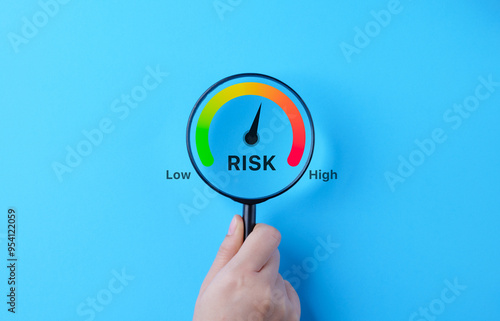 Business Risk Gauge with Low to High Indicator. A hand holding magnifying glass over a risk gauge, showing a scale from low to high, symbolizing the concept of business risk assessment and management.