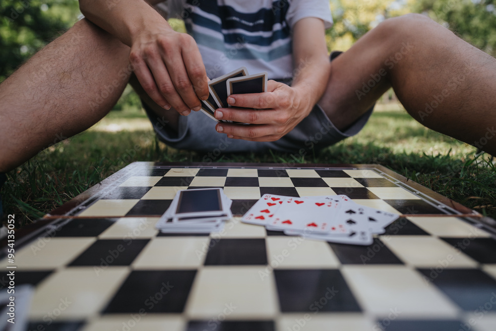 A person enjoys a game of cards on a chessboard outside on a sunny day, evoking leisure and strategy. A person enjoys a game of cards on a chessboard outside on a sunny day, evoking leisure and strategy.