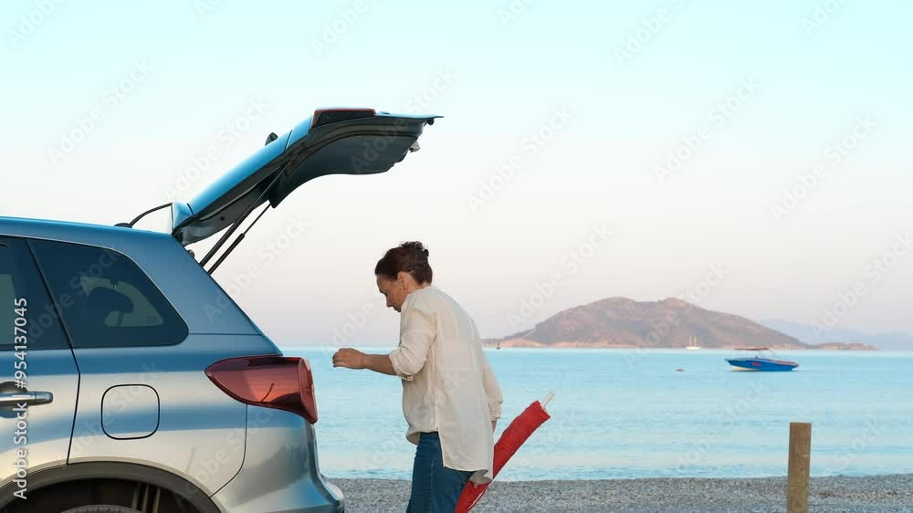 Millennial takes things from trunk in nature. A woman takes her traveling things and put its on the car trunk on the river bank after camping. Millennial takes things from trunk in nature. A woman takes her traveling things and put its on the car trunk on the river bank after camping.