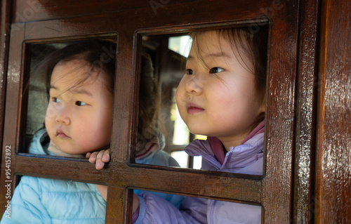 Two young girls are looking out a window