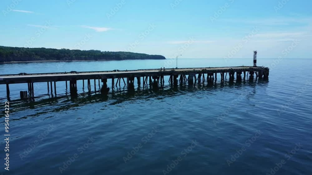 Vieux quai suspendu sur des poutres d'acier au-dessus d'une baie d'eau calme reflétant le bleu du ciel avec une pointe de terre en arrière-plan. ( Baie-des-Chaleurs, Québec ) Vieux quai suspendu sur des poutres d'acier au-dessus d'une baie d'eau calme reflétant le bleu du ciel avec une pointe de terre en arrière-plan. ( Baie-des-Chaleurs, Québec )