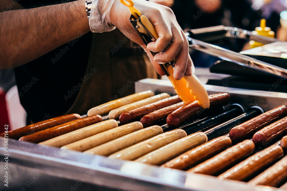 A vendor fries sausages at a hot dog stand.
