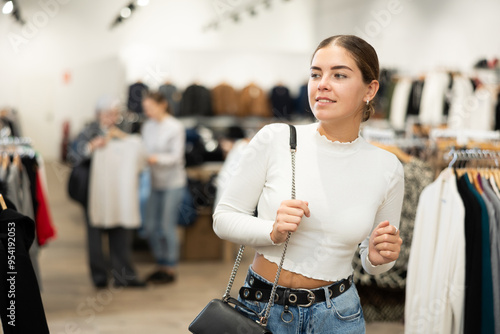 Pleased young girl watching excitedly large stock of clothes in retail outlet photo