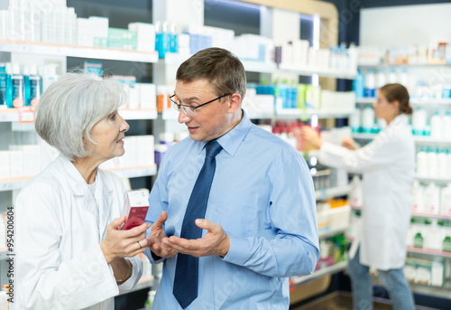 Elderly pharmacist woman communicates with male client and talks about advantages of moisturizing cream for face skin