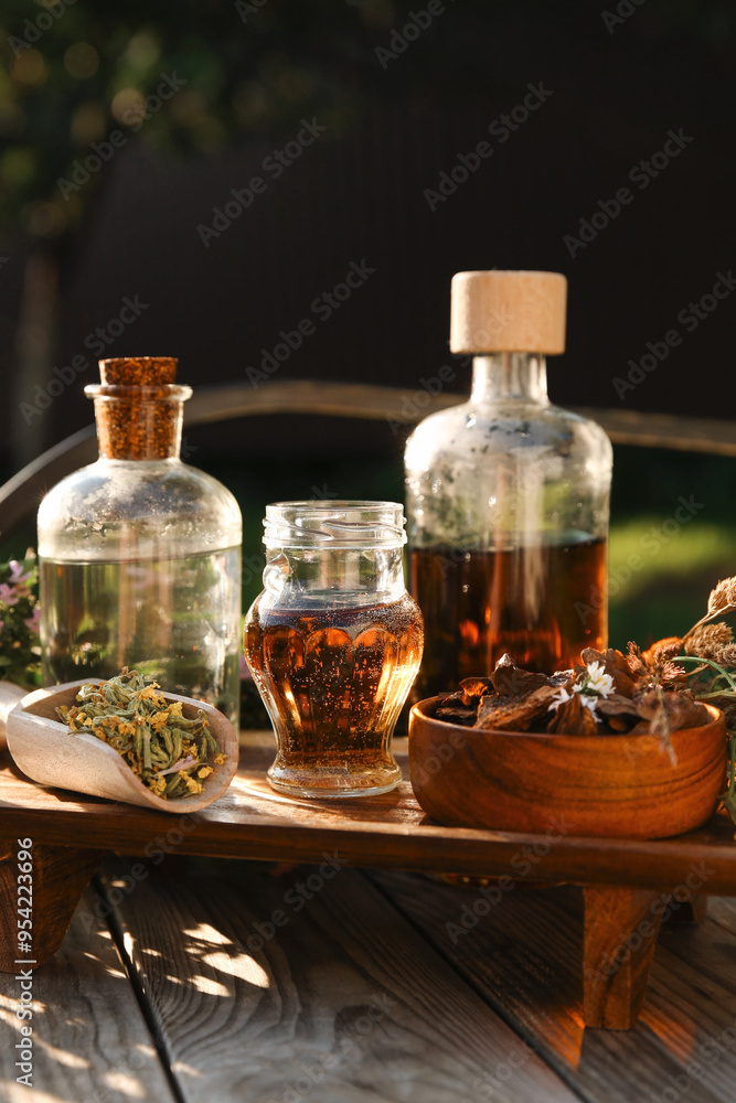 Different tinctures in bottles, bark chips and flowers on wooden bench outdoors, closeup Different tinctures in bottles, bark chips and flowers on wooden bench outdoors, closeup