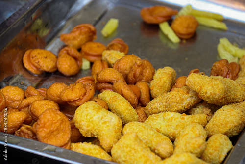 Closeup of golden fried nuggets and crispy fried meatballs served on a metal tray. The nuggets are breaded and perfectly browned, while the meatballs are evenly fried, showcasing a popular food