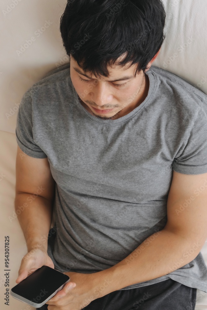 Vertical photo of asian man using mobile phone while relaxing and sitting on white sofa in room at home at day time. Vertical photo of asian man using mobile phone while relaxing and sitting on white sofa in room at home at day time.