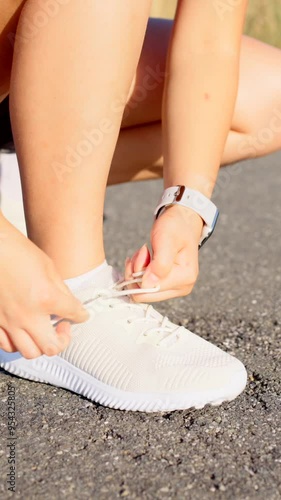 Closeup of unrecognisable woman tying sport shoe laces on a road. Runner getting ready to train.