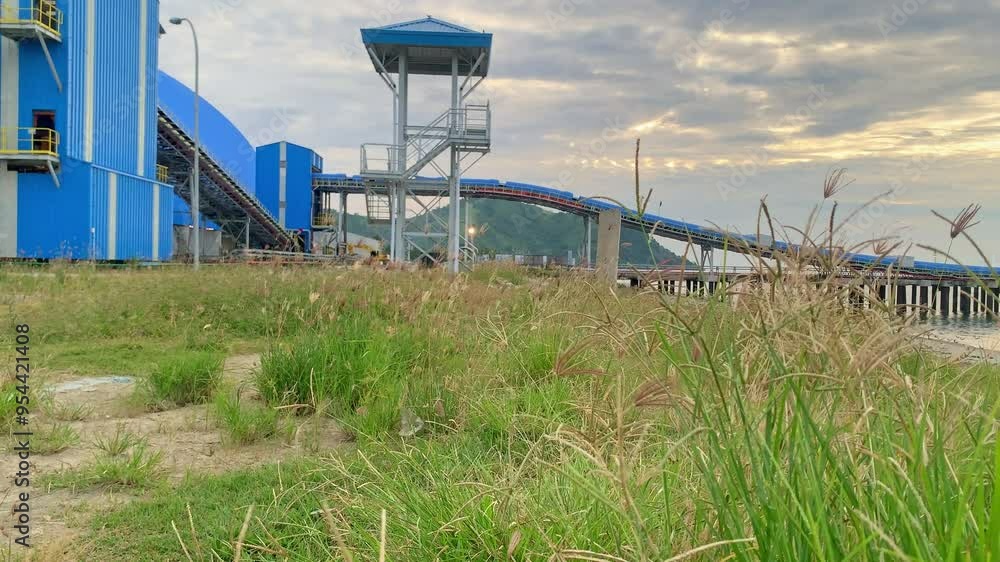 Industrial Structure with Grassy Foreground. A large industrial structure with a long conveyor belt, in a grassy area with a view of the water. Industrial Structure with Grassy Foreground. A large industrial structure with a long conveyor belt, in a grassy area with a view of the water.