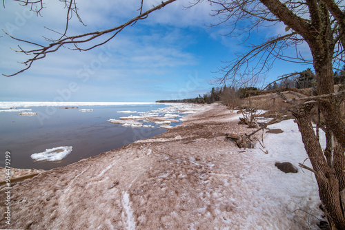 The snow-covered icy beach in the sunny warm last winter day awaits the arrival of spring. Melts ice and snow