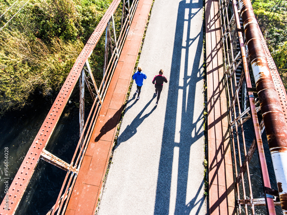 Fototapeta premium Aerial view of a runner running across bridge over the river. Morning running training.