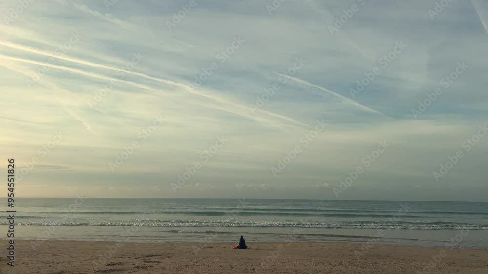 A lone person sits on the beach, gazing at the distant sea horizon. The scene, set in coastal Spain, embodies peace and serenity, capturing a sense of solitude and calm reflection. A lone person sits on the beach, gazing at the distant sea horizon. The scene, set in coastal Spain, embodies peace and serenity, capturing a sense of solitude and calm reflection.