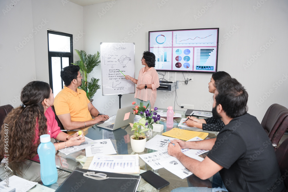 young indian woman discussing about company sales growth whiteboard presentation to colleagues in boardroom. Start up, leadership presentation, business, and workplace concept. young indian woman discussing about company sales growth whiteboard presentation to colleagues in boardroom. Start up, leadership presentation, business, and workplace concept.