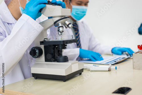 A modern laboratory scene showcasing scientists, both male , in lab coats, analyzing samples using microscopes and computers.