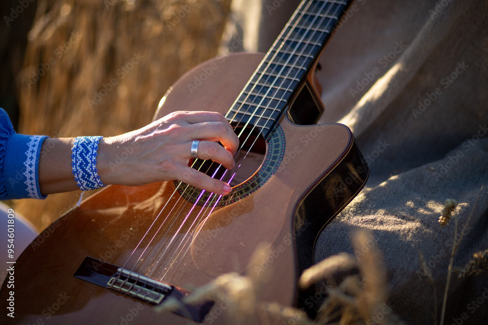 Fototapeta premium A woman's hand plucks the nylon strings of a guitar in the ears of wheat