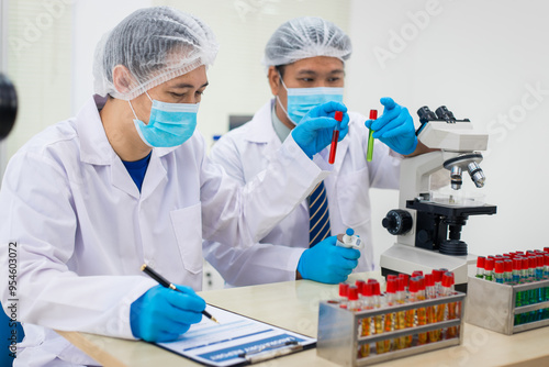 A modern laboratory scene showcasing scientists, both male , in lab coats, analyzing samples using microscopes and computers.