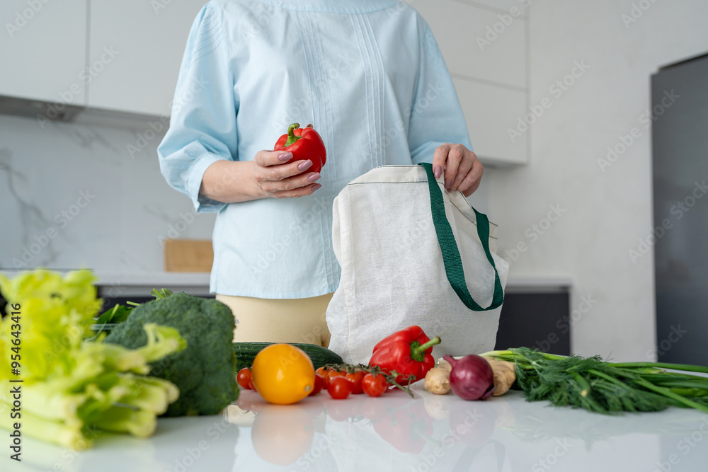 In a contemporary kitchen, a woman is unloading fresh groceries using ecofriendly bags In a contemporary kitchen, a woman is unloading fresh groceries using ecofriendly bags