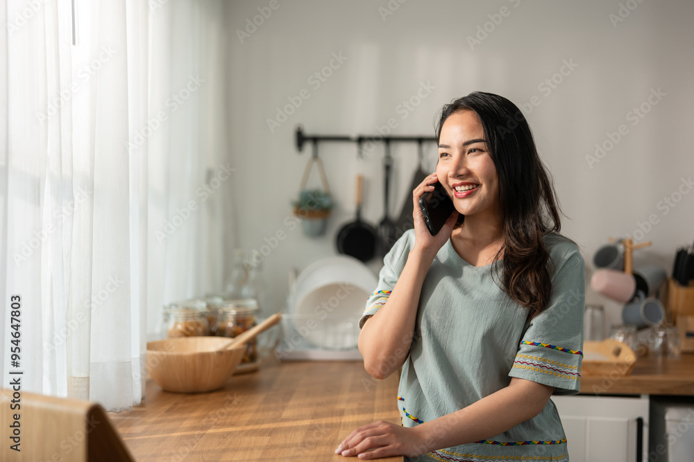 Asian attractive woman talking on mobile phone device in kitchen at home. Asian attractive woman talking on mobile phone device in kitchen at home.