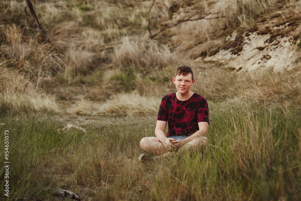 Adolescent boy sitting in grass in the Australian bush Adolescent boy sitting in grass in the Australian bush