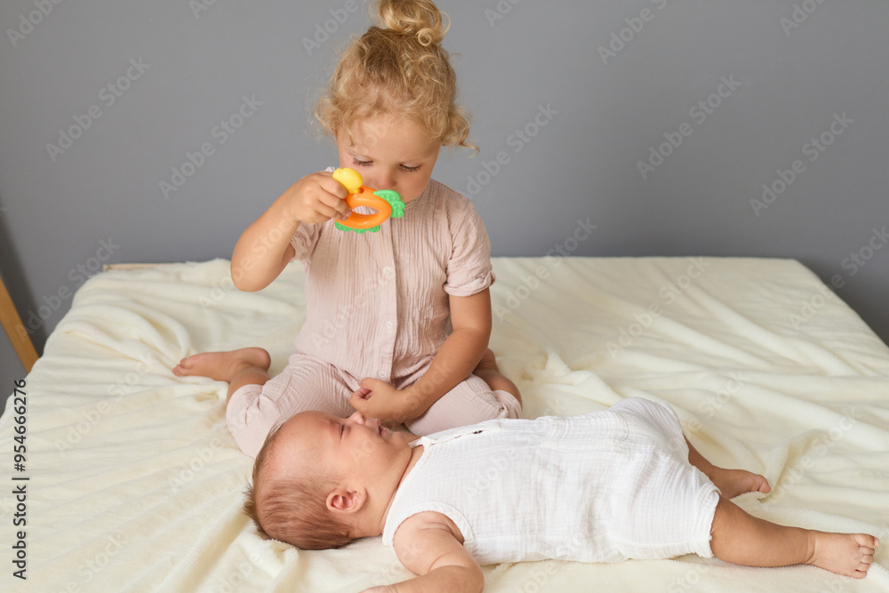 Little Caucasian wavy haired girl soothing her newborn brother who crying by gently bouncing him showing colorful toy to calm him down and comfort him Little Caucasian wavy haired girl soothing her newborn brother who crying by gently bouncing him showing colorful toy to calm him down and comfort him