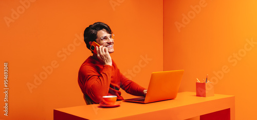 Business consultant in a vibrant orange monochromatic space, handling a client call and using a laptop