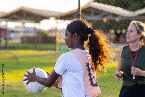 aboriginal girl catching netball with Caucasian umpire or coach in background photo