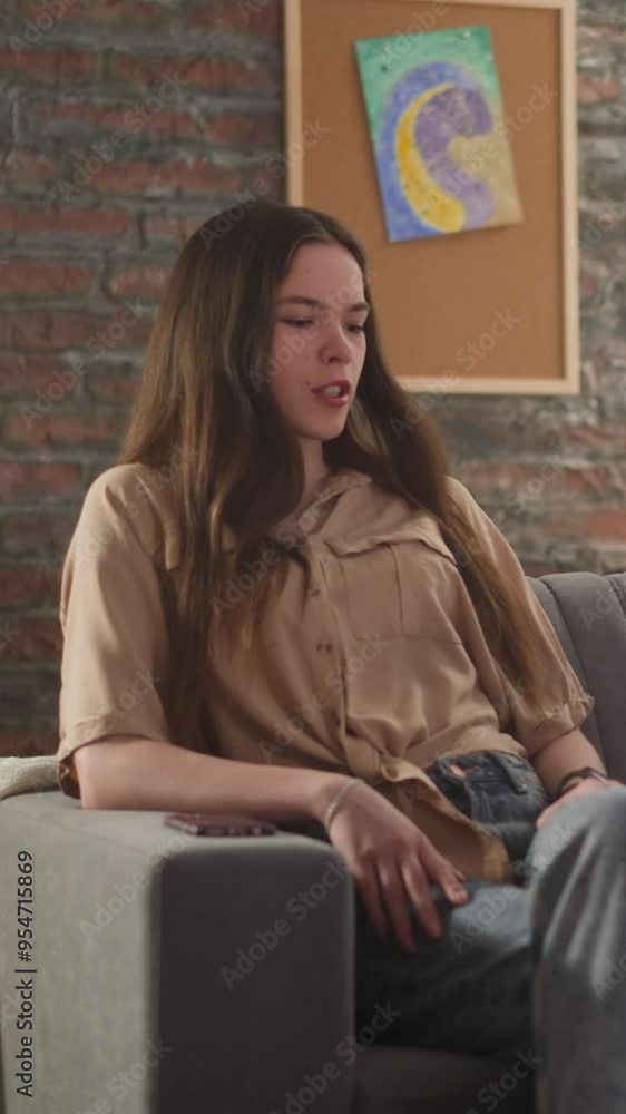 Pretty young woman and long haired man talk sitting together on sofa at sports game broadcasting. Couple of football fans spends time in living room